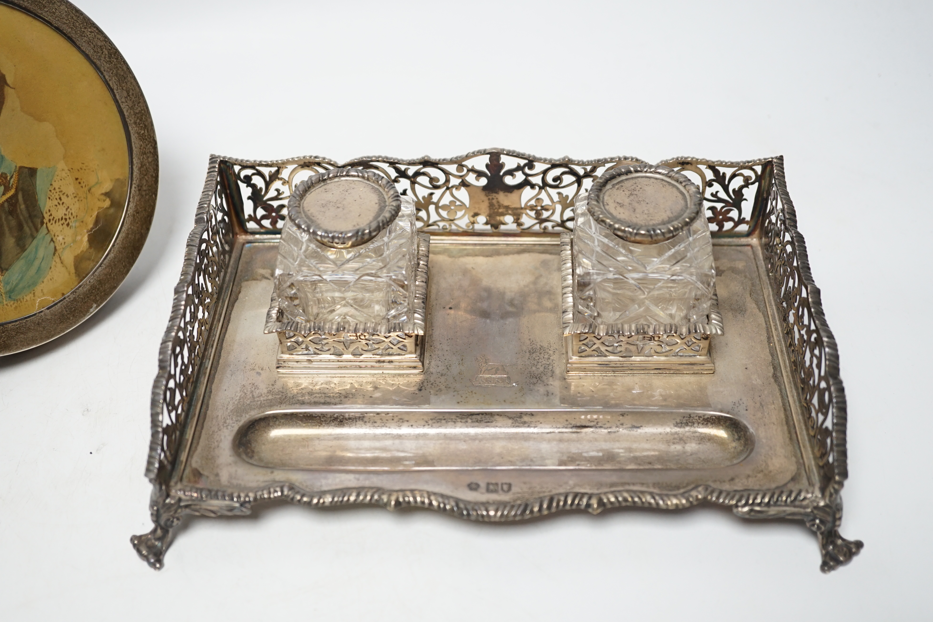 An Edwardian silver rectangular inkstand with pierced three quarter gallery and two mounted cut glass wells, William Hutton & Sons Ltd, London, 1905, 22.3cm and a George V silver mounted circular photograph frame.